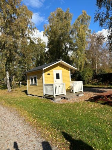 a small yellow cabin with a porch in a park at Alholmens camping in Sölvesborg