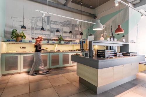 a woman walking through a kitchen in a restaurant at MEININGER Hotel Berlin Airport in Berlin