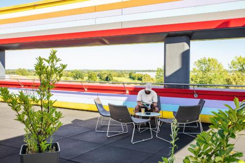 a man sitting at a table in front of a building at MEININGER Hotel Berlin Airport in Berlin