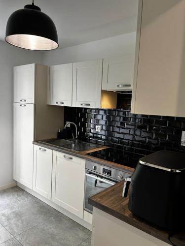 a kitchen with white cabinets and a black tile wall at Maison Jazharra -SPA - 6 - 8 pers - Proche Golf in Frehel