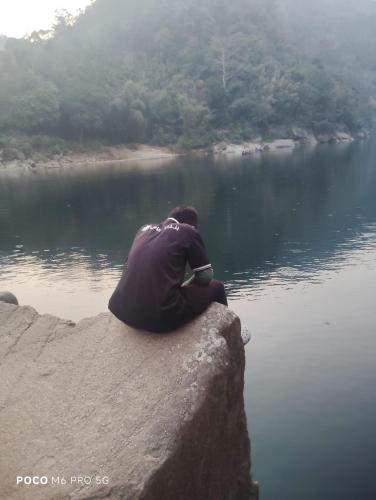 a man sitting on a rock near a body of water at Meban camping shnongpdeng in Dawki