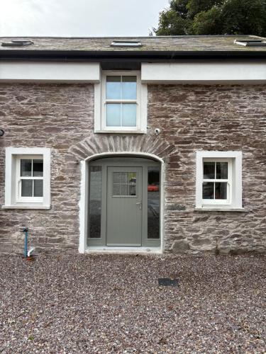 a brick house with a gray door and two windows at The Courtyard Apartments in Macroom