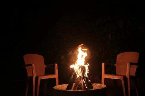 a fire pit with two chairs and a fire burns at Janhavi Homestay in Napoklu