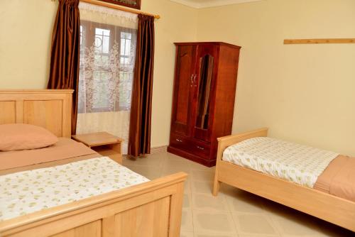 a bedroom with two beds and a wooden cabinet at Aida's Gardens And Mable's Kitchen Entebbe in Entebbe