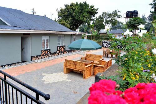 a patio with benches and an umbrella and flowers at Aida's Gardens And Mable's Kitchen Entebbe in Entebbe