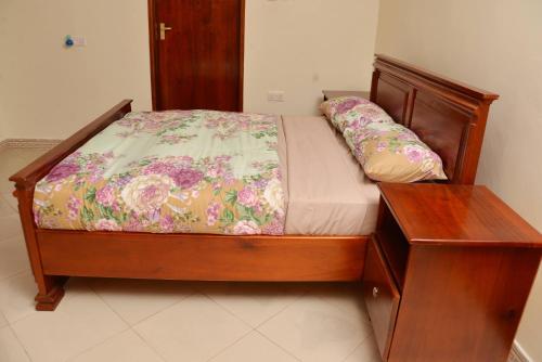 a small bed with a wooden frame and a wooden table at Aida's Gardens And Mable's Kitchen Entebbe in Entebbe