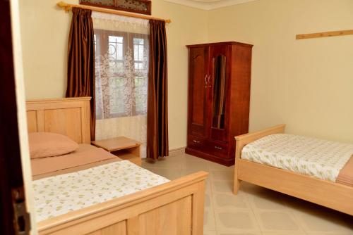 a bedroom with two beds and a dresser and a window at Aida's Gardens And Mable's Kitchen Entebbe in Entebbe