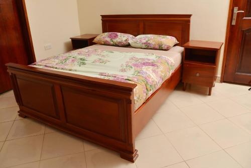 a bedroom with a wooden bed with a floral bedspread at Aida's Gardens And Mable's Kitchen Entebbe in Entebbe