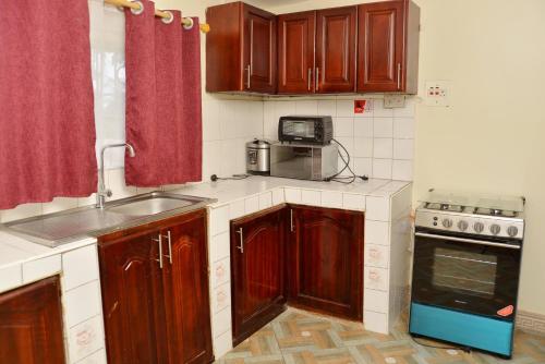 a kitchen with wooden cabinets and a sink and a stove at Aida's Gardens And Mable's Kitchen Entebbe in Entebbe