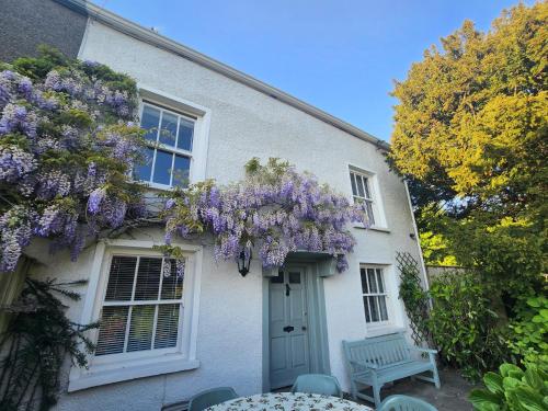 a white house with a wreath of purple flowers on it at Bridge End Cottage in Ulverston