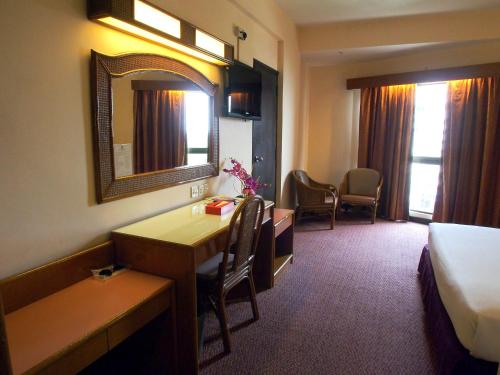 a hotel room with a desk and a bed and a mirror at Hotel Grand Continental Langkawi in Kuah