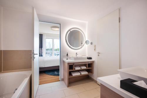 a bathroom with a tub and a sink and a mirror at Lindner Hotel Boltenhagen, part of JdV by Hyatt in Boltenhagen