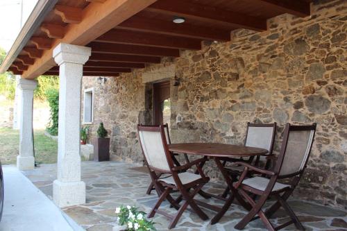 a wooden table and chairs on a patio with a stone wall at CASA PEINADO in Boimorto