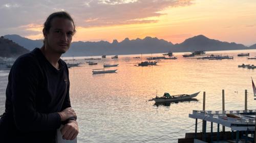 a man standing next to a body of water with boats at Rusde's Komodo Homestay in Pulau Komodo