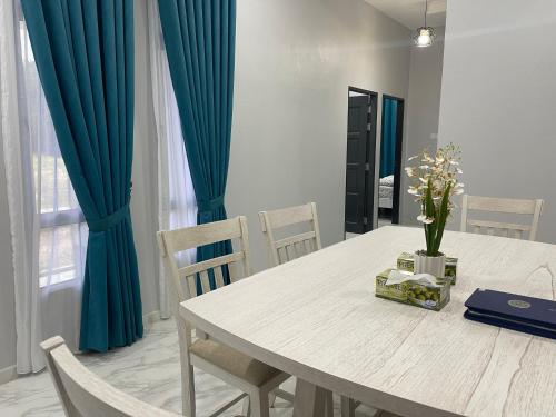 a dining room with a white table and blue curtains at Eleeya Guest House in Ketereh
