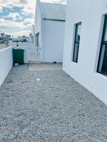 a house with a gravel driveway next to a white building at 44 Staycation Beach-house in Britannia Bay