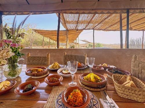 a wooden table with plates of food and wine glasses at Agafay, La Ferme Nomade Bivouac in El Karia