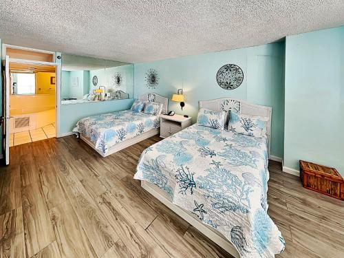 two beds in a bedroom with blue walls and wooden floors at The Salty Fountain in Seabreeze