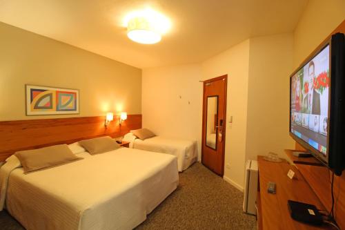 a hotel room with two beds and a flat screen tv at Pousada Villa Capivary Campos do Jordão in Campos do Jordão