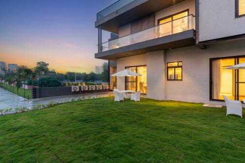 a house with a lawn with two tables and umbrellas at Gardenia 4-BHK Farmhouse with Private Pool, Game Zone, & Lush Garden in Dera Māndi