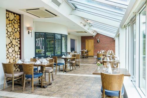 a dining room with tables and chairs and windows at Macdonald Craxton Wood Hotel & Spa in Ledsham