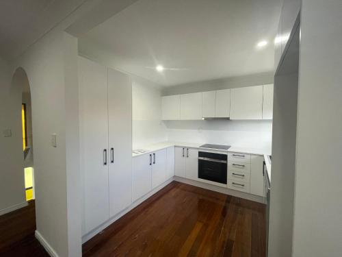 a white kitchen with white cabinets and a wooden floor at Sunnybank Hills Home - Near Shopping & Dining in Brisbane