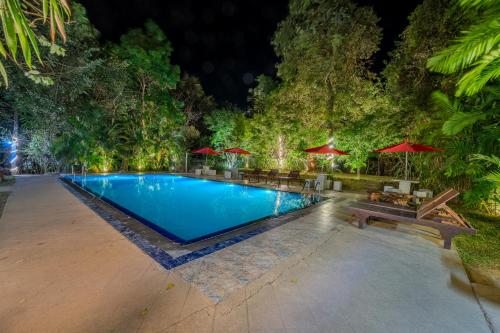 a swimming pool with benches and umbrellas at night at woodland sanctuary in Habarana