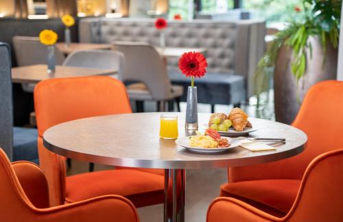 a table with a plate of food and orange chairs at Leonardo Hotel Vienna Hauptbahnhof in Vienna