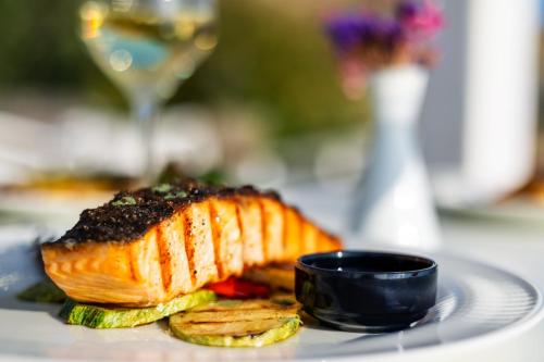 a plate of food with a piece of fish and a glass of wine at San Marco Hotel and Villas in Houlakia