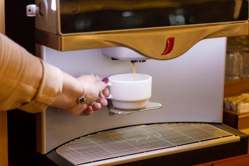 a person is pouring a cup into a coffee machine at ibis Styles Fortaleza Shopping Giga Mall in Fortaleza