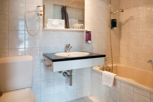 a bathroom with a sink and a toilet and a tub at Strandhotel Seeblick in Faulensee
