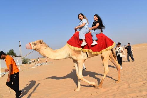 a group of people riding on a camel in the desert at Open Sky Overnight Campsite in Desert Safari Buffet BBQ Entertainments Drinks Bone Fire 4x4 Dune Bashing in Dubai
