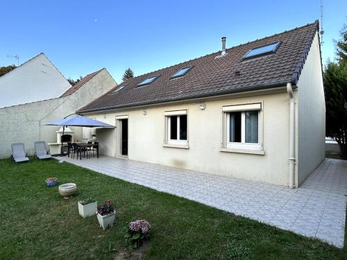 Verneuil-lʼÉtangにあるJolie et charmante maison accessible depuis Parisのパティオ(テーブル、傘付)が備わる家