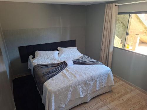 a bedroom with a bed with white sheets and a window at Apartamento para família in Guarapuava