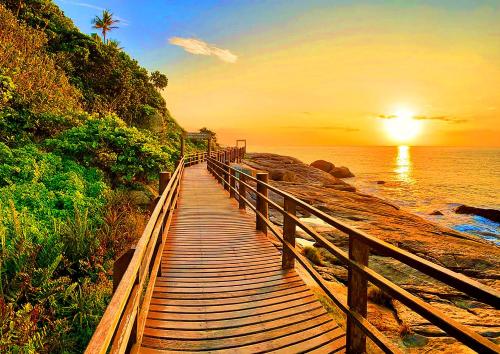 a wooden boardwalk leading to the ocean at sunset at Suítes Suarão in Itanhaém