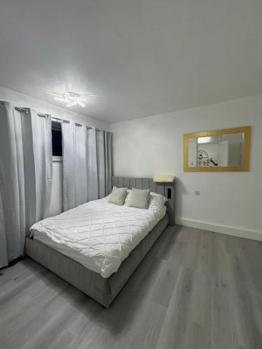 a bedroom with a bed with white sheets and curtains at Newly Refurbished - Stylish - Modern - And Cosy Flat - King Size Bed with Built In Speakers - Bedside Lamp - And USB Ports - Sofa Bed - In Islington North London in London