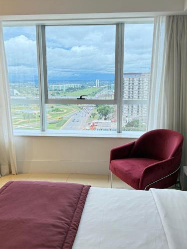 a bedroom with a bed and a chair and a large window at Fabuloso Hotel Alvorada - Apt da Rede Premium in Brasilia