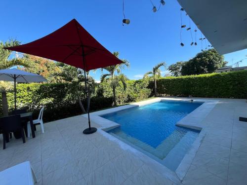a swimming pool with a red umbrella and a table at Sunset Private Villa in Ricaurte in Llano del Pozo