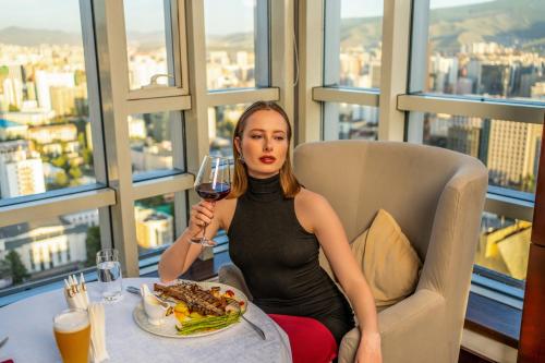 a woman sitting at a table with a glass of wine at Best Western Premier Tuushin Hotel in Ulaanbaatar