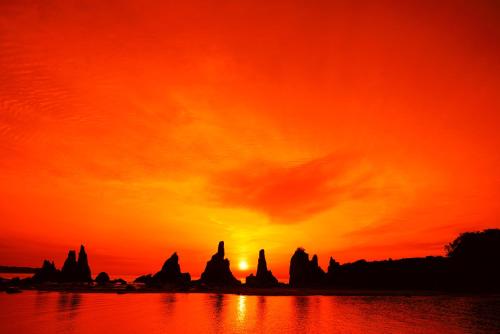 an orange sunset with rocks in the water at 1日ひと組 一棟貸の宿 癒し宿かぐら in Kushimoto