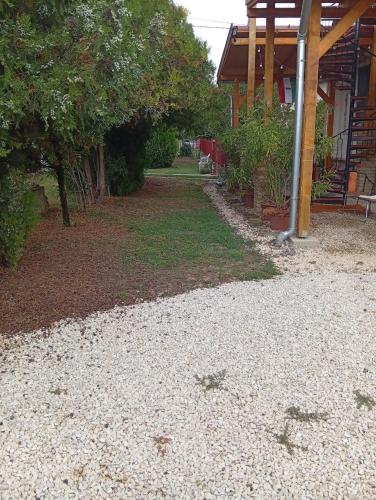 a gravel yard with a house and trees and a building at Hagyományőrző és múltidéző porta in Báta