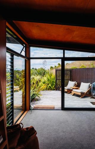 an open door to a patio with two lounge chairs at Whare Tatū in Raglan