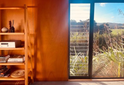 a room with a sliding glass door with a window at Whare Tatū in Raglan