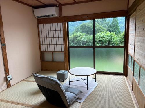 a room with a chair and a table and a large window at ゲストハウス八咫 in Tanabe