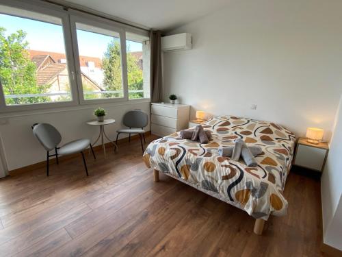 a bedroom with a bed and two chairs and windows at Studio climatisé 30 m2 à 2 min de Colmar in Horbourg