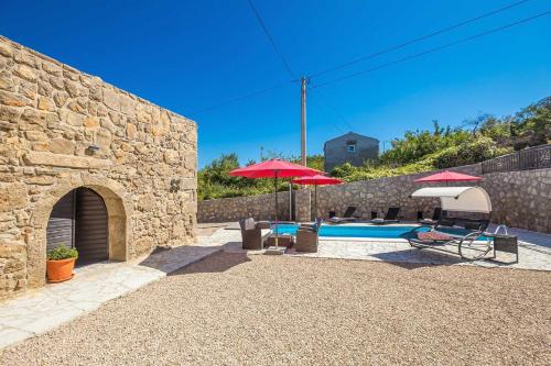 a stone building with a pool and umbrellas at Villa Mediteran with private pool in Vrh