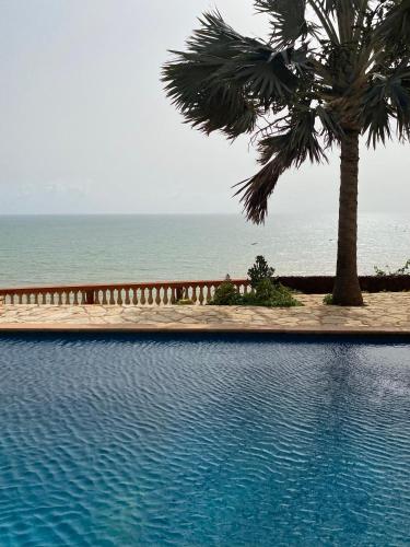 einen Pool mit einer Palme und dem Meer in der Unterkunft Maison Atlantique in Rufisque