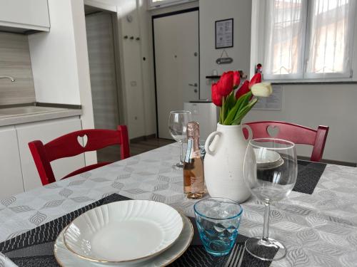 a table with a white vase with red flowers and glasses at Sweet Home - Wi-fi Gratuito in Monza