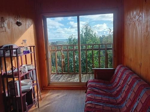 a living room with a couch and a large window at Refugio de montaña con vista al mar in Curiñanco
