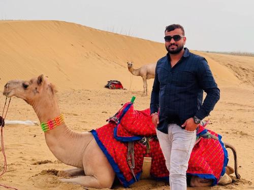 a man standing next to a camel in the desert at Hotel Robin Jaisalmer Near fort view in Jaisalmer